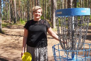 Nainen poseeraa frisbeegolfmaalin äärellä.